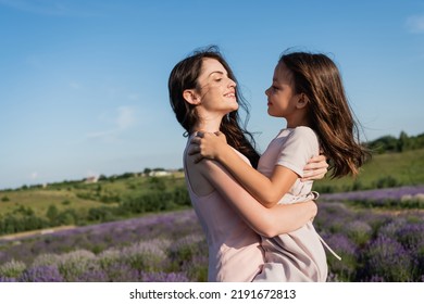 Side View Of Brunette Mom And Daughter With Long Hair Hugging In Field