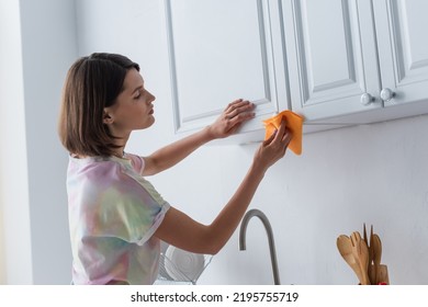 Side View Of Brunette Woman Cleaning Cupboard In Kitchen At Home