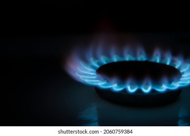 Side View Of Burning Gas Stove With Blue Flame In Dark Kitchen. Black Background. Copy Space For Your Text. Selective Focus. Biogas Or Natural Gas. Fuel Industry Theme.