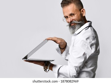 Side View Of The Business And Fashion Mature Bearded Man In A White Shirt With A Sly Smile Closes The Laptop On A Gray Background. Successful Completion Concept.