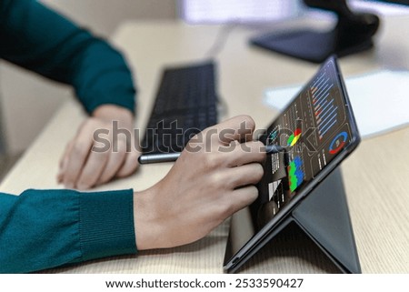 Side view of a business man using a tablet in the office with a pen, analyzing some digital graphics , online work concept