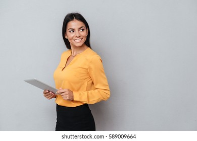 Side View Of Business Woman In Suit Which Holding Tablet Computer And Looking Away. Isolated Gray Background