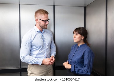 Side View Of A Businessman And Businesswoman Standing In Elevator Talking With Each Other