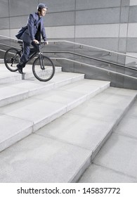 Side View Of A Businessman In Crash Helmet Riding Bicycle Down Steps