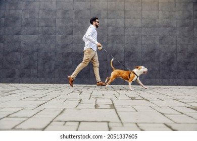 Side View Of A Businessman Dressed Smart Casual Running With His Dog. A Dog On A Leash Running While The Man Is Trying To Catch Up With It. A Man Running With His Dog