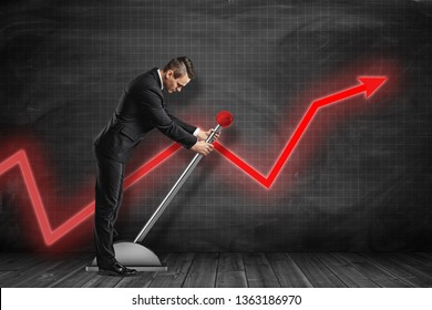 Side view of businessman looking down and pulling big lever near black graph ruled wall with red graph arrow on it. Jumpstart your business. Work hard. Achieve success. - Shutterstock ID 1363186970