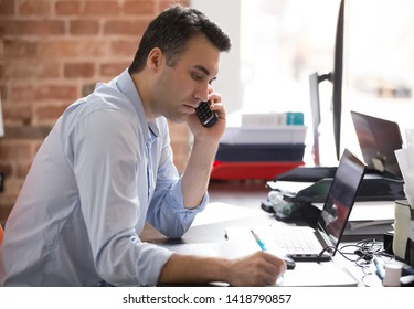 Side view businessman sitting at desk in office holds phone make business call listen client writing notes feels confident concentrated, busy working day, solve problem distantly, hr workforce concept - Powered by Shutterstock