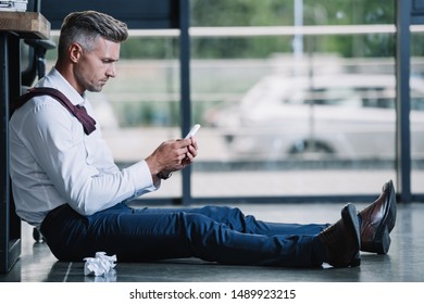 side view of businessman sitting on floor and using smartphone 