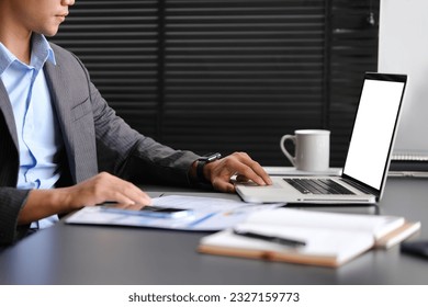 Side view of businessman working with financial document and using laptop computer at workplace - Shutterstock ID 2327159773