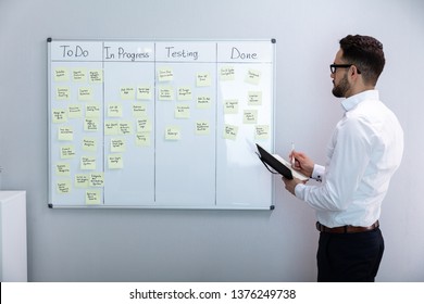 Side View Of Businessman Writing On Sticky Notes Attached To White Board In Office