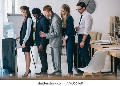 Side View Of Businesspeople Standing In Queue For Water Dispenser At Office