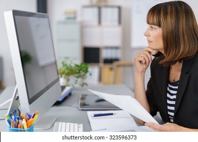 Side View Of A Businesswoman Looking At Her Computer Screen Seriously While Holding Documents.