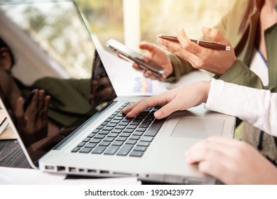 Side View Of Businesswoman's Hands Using Laptop Computer Placed On Messy Office Desktop. Teamwork With Business People Analysis Cost Graph On Desk At Meeting Room.