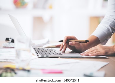 Side view of businesswoman's hands using laptop computer placed on messy office desktop