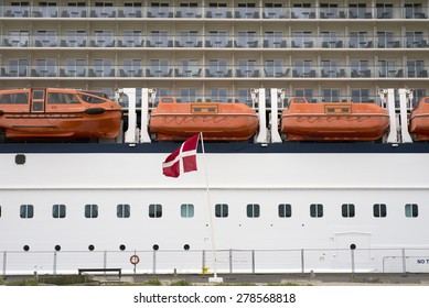 Side View Of Cabins On Cruise Liner With Lifeboats And Danish Flag Blowing In Tge Wind On Fredericia Harbor. No People And Ship Are Unrecognizable.