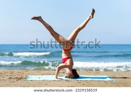Side view of calm female in bikini performing Tripod Headstand while having session alone on coast of ocean