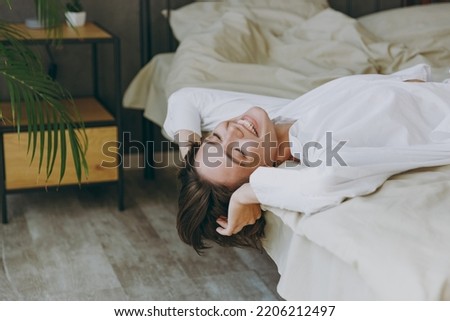 Side view calm fun young woman wear white shirt pajama she lying in bed close eyes rest relax spend time in bedroom lounge home in own room hotel wake up dream in good mood day Real estate concept.
