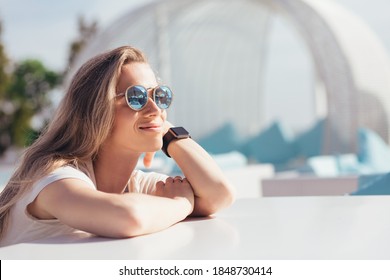 Side view of a calm relaxing beautiful young woman sitting at a table in an outdoor white stylish cafe and enjoying the sun while traveling on sunny warm summer day. Concept of long-awaited vacation - Powered by Shutterstock