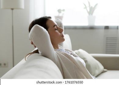 Side View Calm Woman Closed Eyes Enjoy Fresh Conditioned Air Rest At Home Leaned On Comfy Couch. No Stress, Relief Tiredness, Fall Asleep At Day Nap. Hands Behind Head Pose Of Deep Relaxation Concept