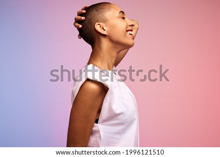 Side view of a carefree woman with shaved head. Confident female with short hair on colorful background.