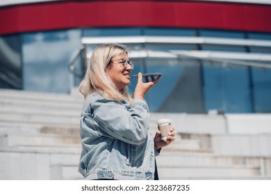 Side view casual clothed blond plus size woman recording audio message on mobile phone at urban background. - Powered by Shutterstock