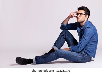 Side View Of A Casual Fashion Man Sitting On Gray Background And Looking Away From The Camera