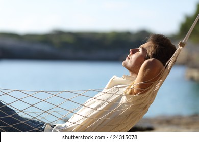 Side view of a casual happy man relaxing on a hammock in the beach on holidays