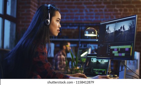 Side view of casual Korean girl wearing headphones and editing video in office working at table