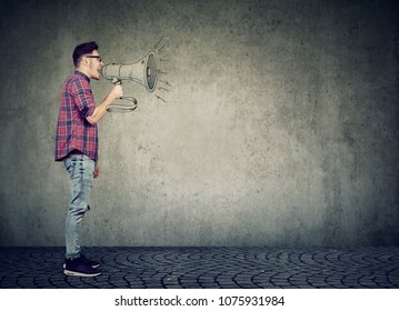 Side View Of Casual Man Speaking With Loudspeaker Giving Speech And Propaganda On Gray Background. 