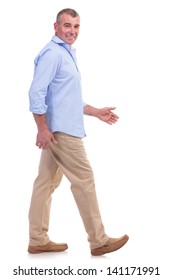 Side View Of A Casual Senior Man Walking Forward And Looking At The Camera. Isolated On White Background