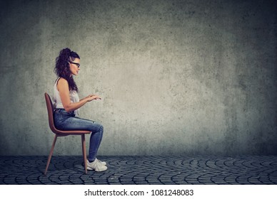 Side view of casual woman sitting at invisible table pretending to type on computer. 