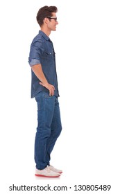 Side View Of A Casual Young Man Standing With His Hands On His Hips And Looking Away From The Camera. Isolated On A White Background