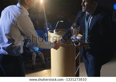 Side view of Caucasian businessman appreciating mixed race business male executive on stage in auditorium