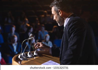  Side View Of Caucasian Businessman Holding Podium Speaker In His Hand At Auditorium