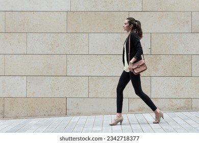 Side view of a Caucasian Businesswoman walking on city street in front of modern marble wall. - Powered by Shutterstock