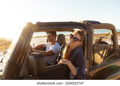 Side view of a Caucasian couple inside an open top car, the man driving, the woman smiling and looking through the window  - Powered by Shutterstock