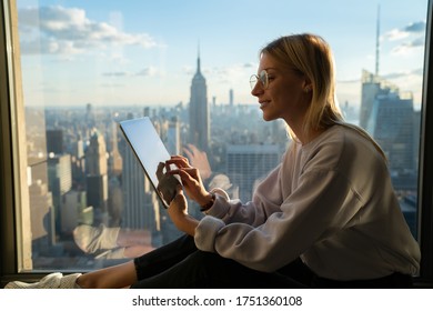 Side View Of Caucasian Digital Nomad Working On Graphic Tablet Sitting Near Scenery Skyline Of Manhattan District, Millennial Female Blogger Installing New Social App For Influence Communication