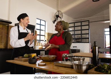 Side view of a Caucasian female chef and an Senior African woman at a cookery class, gesturing and laughing while the chef instructs the woman, preparing food in a mixing bowl  - Powered by Shutterstock