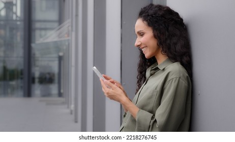 Side View Caucasian Hispanic Woman 30s Businesswoman Holding Cell Phone Standing Near Wall Building Outdoors Success Good News Mobile App Win Surprised Lady Celebrating Victory On Smartphone Triumph