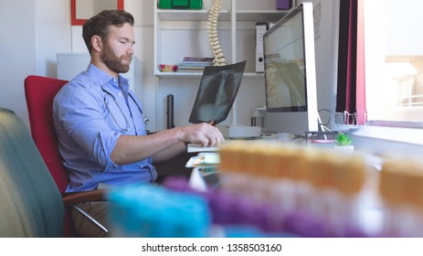 Side View Of Caucasian Male Doctor Checking  X Ray Report In Computer At Clinic 