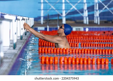 Side View Of Caucasian Male Swimmer At Swimming Pool, In Water Holding Onto S Starting Block, Starting A Backstroke Race