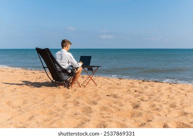 Side view of Caucasian man using laptop while sitting in sun lounger on beach on sunny day. Guy in white shirt working on laptop at sea, freelancer in world time - Powered by Shutterstock