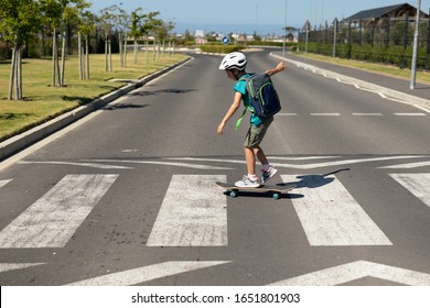 Side view of a Caucasian school boy wearing a cycling helmet crossing the road on a pedestrian crossing on a skateboard, on his way to elementary school on a sunny day - Powered by Shutterstock