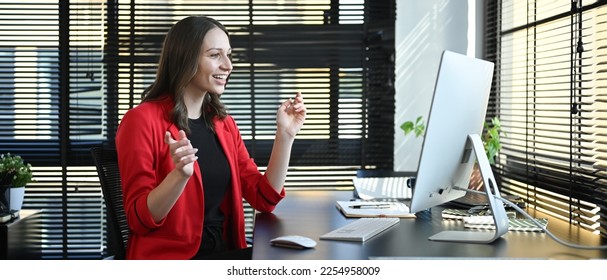 Side view of caucasian woman corporate CEO in red luxury suit watching online webinar on computer in modern office - Shutterstock ID 2254958009