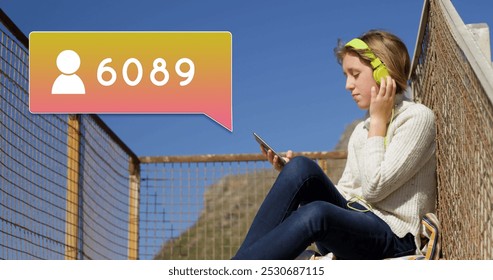 Side view of a Caucasian woman wearing headphones sitting on a stairway. She is taking a selfie beside a follow icon and increasing numbers on a yellow gradient chat box 4k - Powered by Shutterstock - Get 15% off with code: PIKWIZARD15