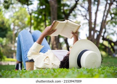 Side view of charming woman reading book in grass under tree with cup of coffee. Relax in summer time holiday laying on the grass field comfortable feeling. - Shutterstock ID 2153947009