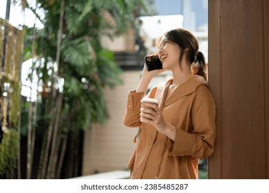 Side view of a cheerful and beautiful young Asian woman enjoys talking on the phone with her friend while relaxing outdoors on a sunny day. Modern life, people and wireless technology concepts - Powered by Shutterstock