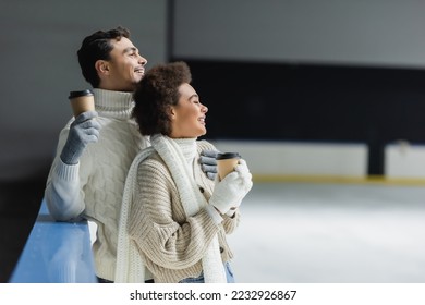Side view of cheerful interracial couple holding coffee to go and looking away on ice rink  - Shutterstock ID 2232926867