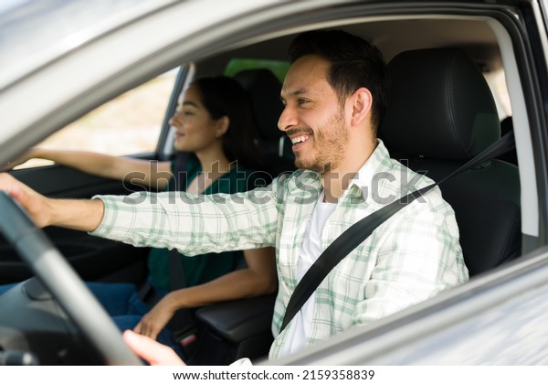 Side view of a cheerful\
latin man driving while laughing with his girlfriend during a fun\
car trip