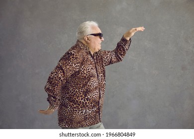 Side View Of Cheerful Rich Fat Senior Man In Leopard Patterned Shirt Dancing In Studio With Gray Background. Happy Positive Stylish Retired Old Guy Having Fun And Doing Funny Egyptian Arm Dance Move